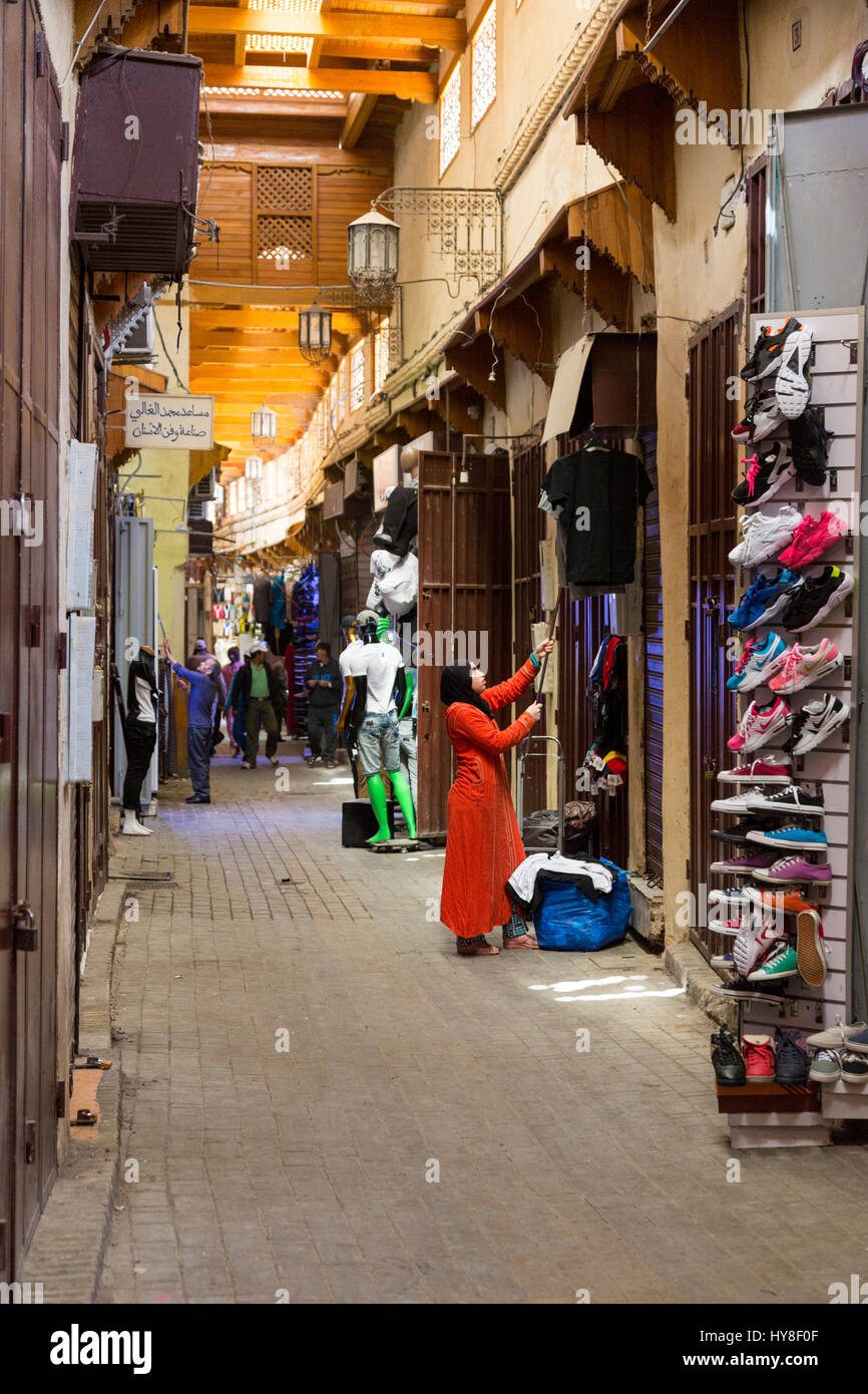 Meknès, Marokko.  Ladenbesitzer hängt ein Hemd auf einem hohen Geländer in der Medina. Stockfoto