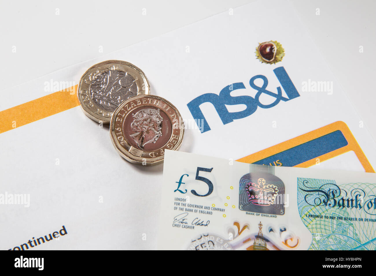 Neue £1 Pfund-Münzen, £2 Pfund-Münzen und £5 Pfund-Noten auf einem Premium Bond-Dokument Stockfoto