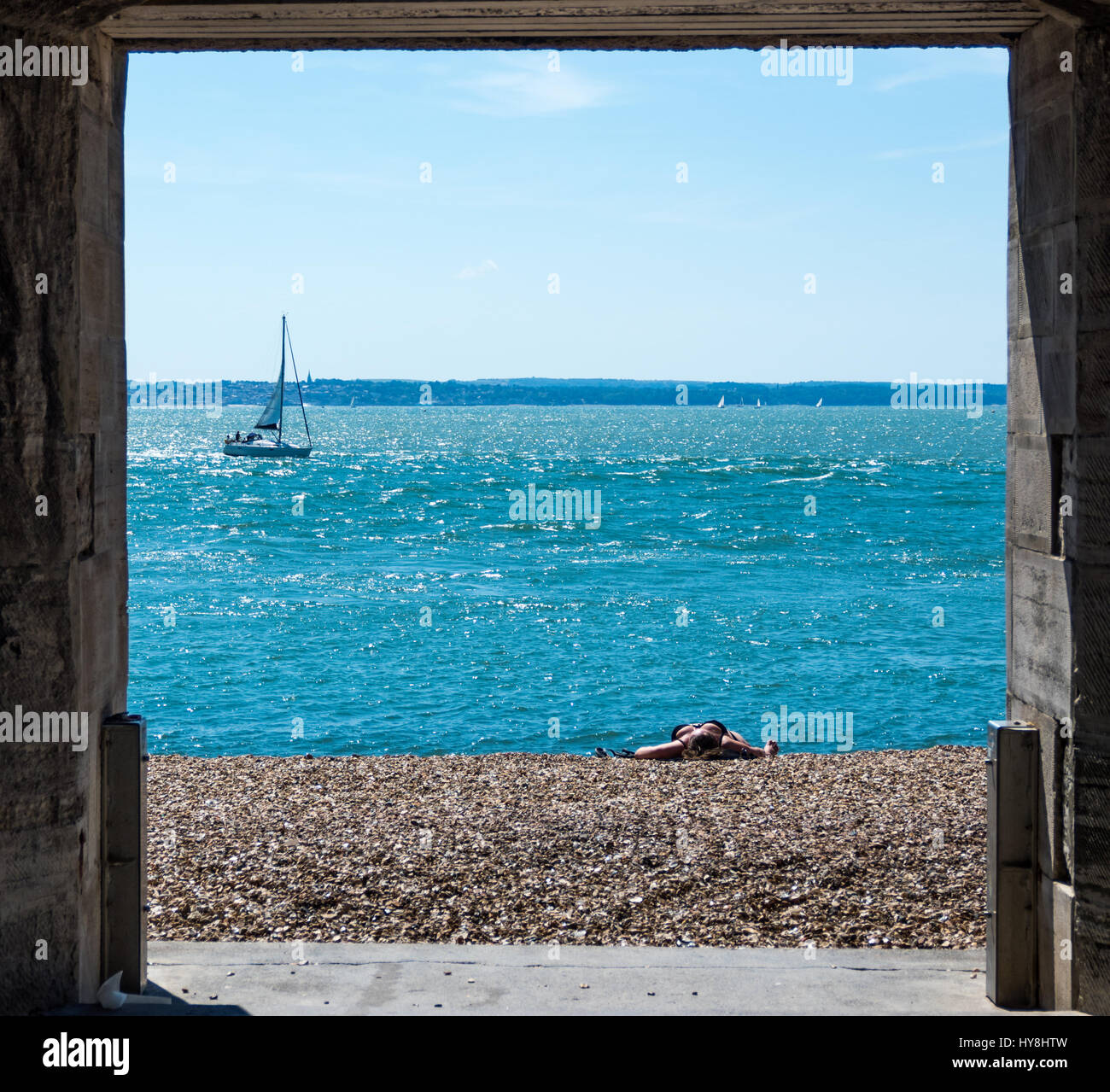 Ein Blick durch die Sally Port in Old Portsmouth mit einer Frau, Sonnenbaden am Strand, während eine Yacht durch segelt Stockfoto