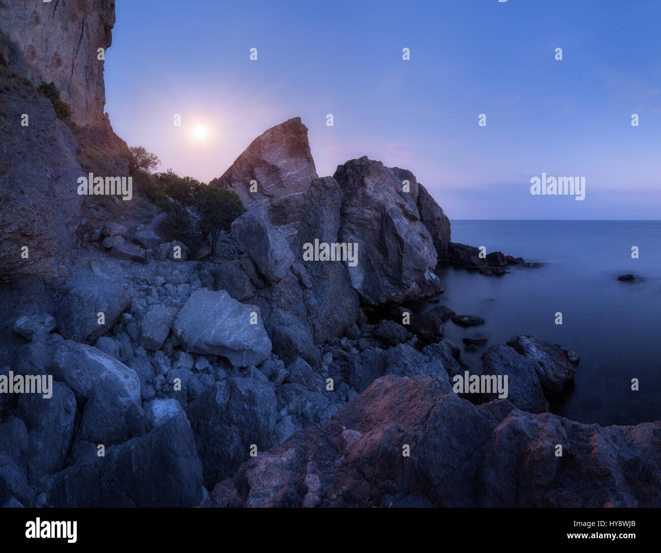 Berglandschaft am Meer in der Nacht. Hohe Felsen und Steinen im Wasser auf dem Hintergrund des blauen Nachthimmel mit Vollmond im Sommer. Erstaunliche Szene auf Stockfoto