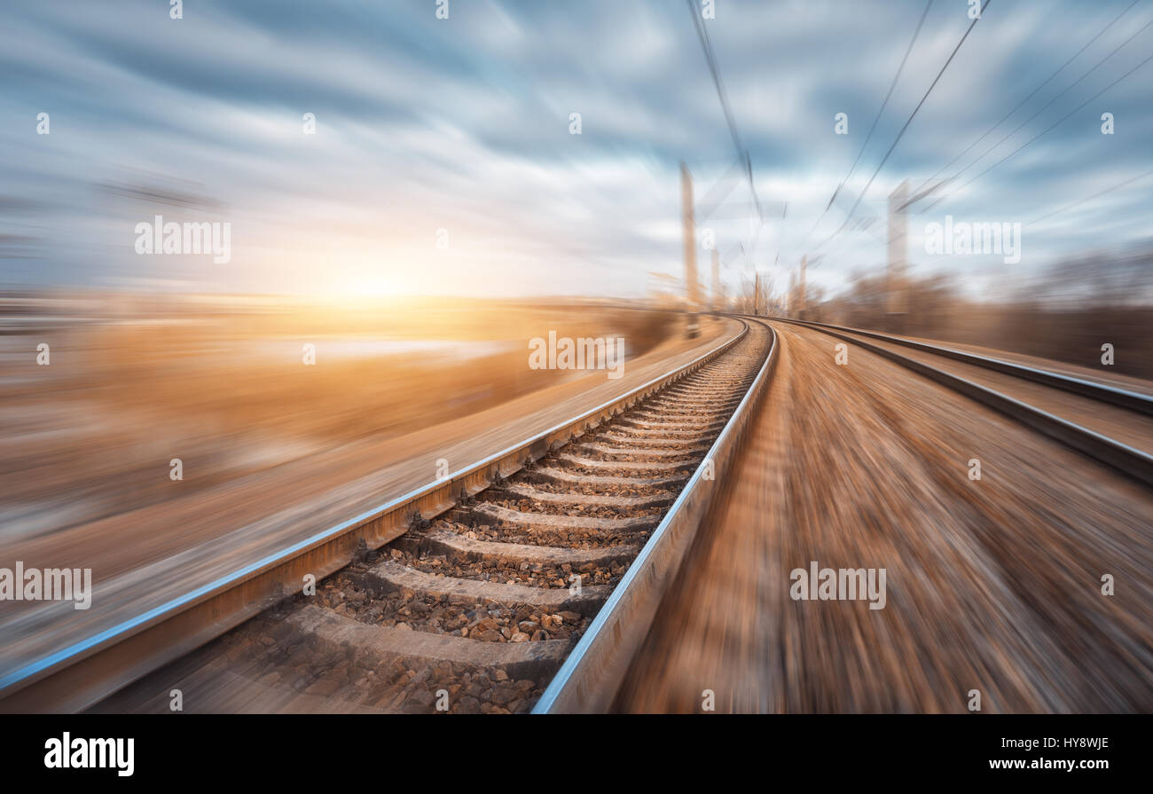 Eisenbahn in Bewegung bei Sonnenuntergang. Bahnhof mit Motion blur Effekt und bunten Himmel mit Wolken. Industrielle Konzept Hintergrund. Eisenbahn Reisen, ra Stockfoto