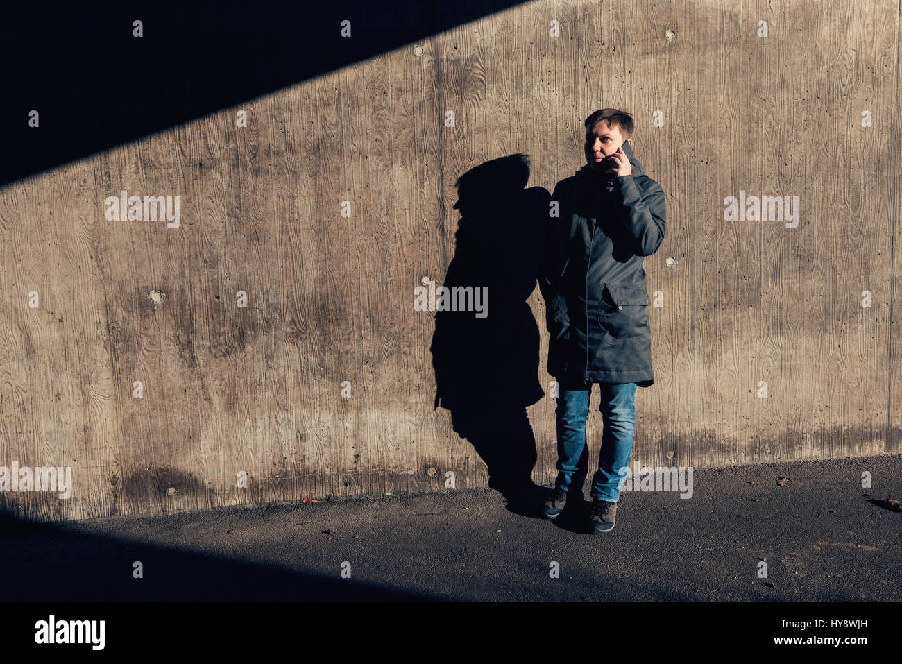 Schwere authentische Frau mit kurzen Haaren, telefonieren mit Handy auf der Straße in die untergehende Sonne contrastly Schattenwurf auf t winter unter Passage, Stockfoto