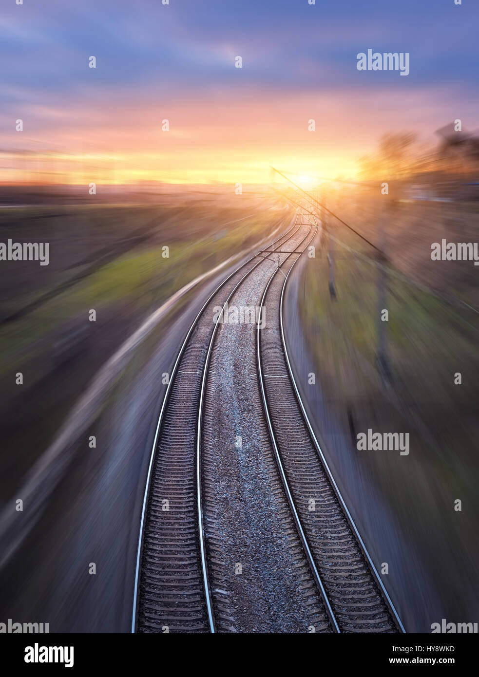 Eisenbahn in Bewegung bei Sonnenuntergang. Bahnhof mit Motion blur Effekt und sonnigen Himmel mit Wolken. Industrielle Konzept Hintergrund. Blick von oben. Rai Stockfoto