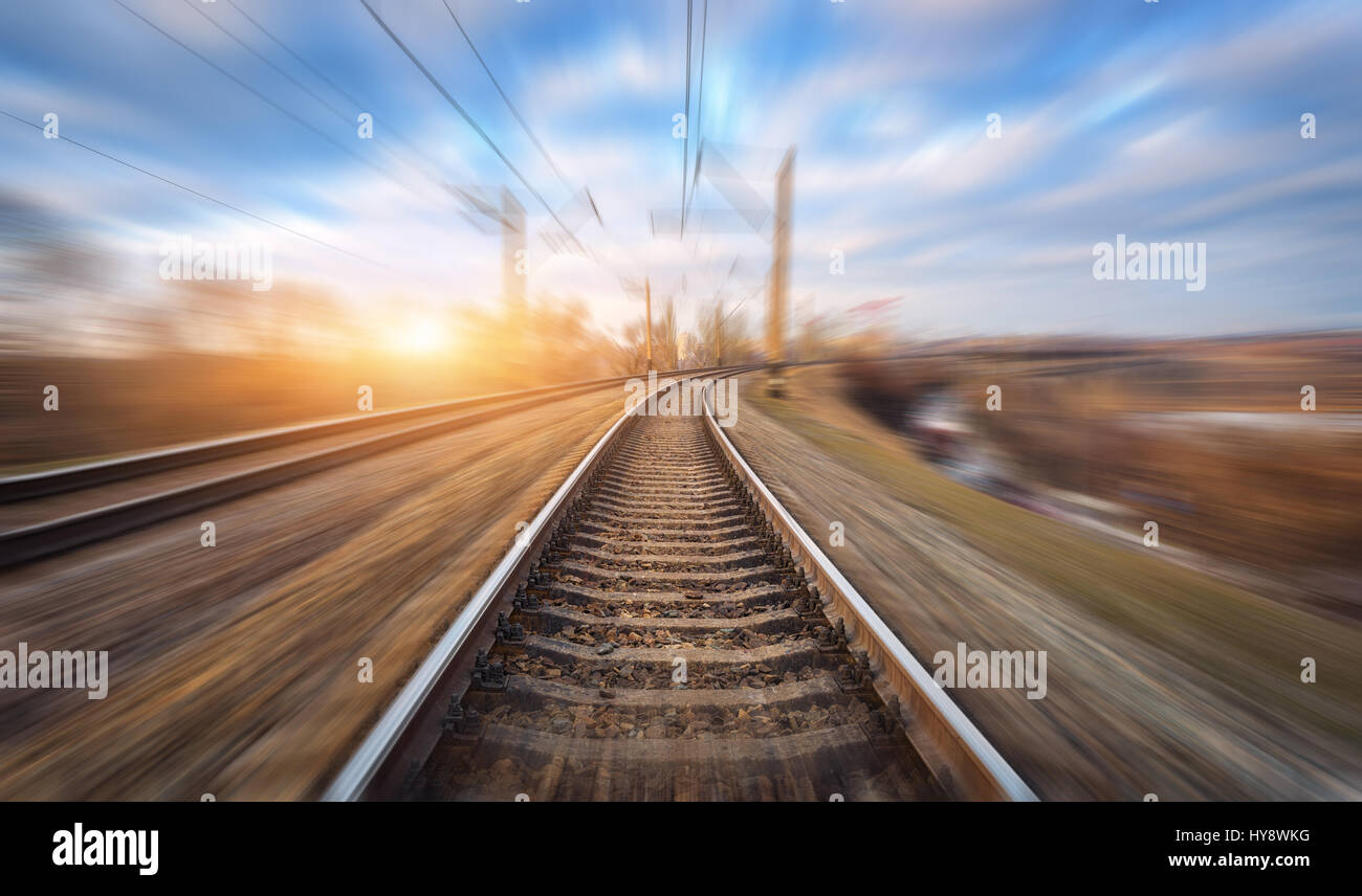 Eisenbahn in Bewegung bei Sonnenuntergang. Bahnhof mit Motion blur Effekt und bunten Himmel mit Wolken. Industrielle Konzept Hintergrund. Eisenbahn Reisen, ra Stockfoto