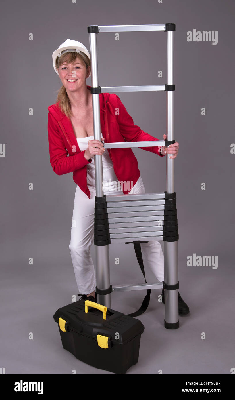Arbeitnehmerin trägt einen Schutzhelm und hält eine Teleskop Leiter Stockfoto