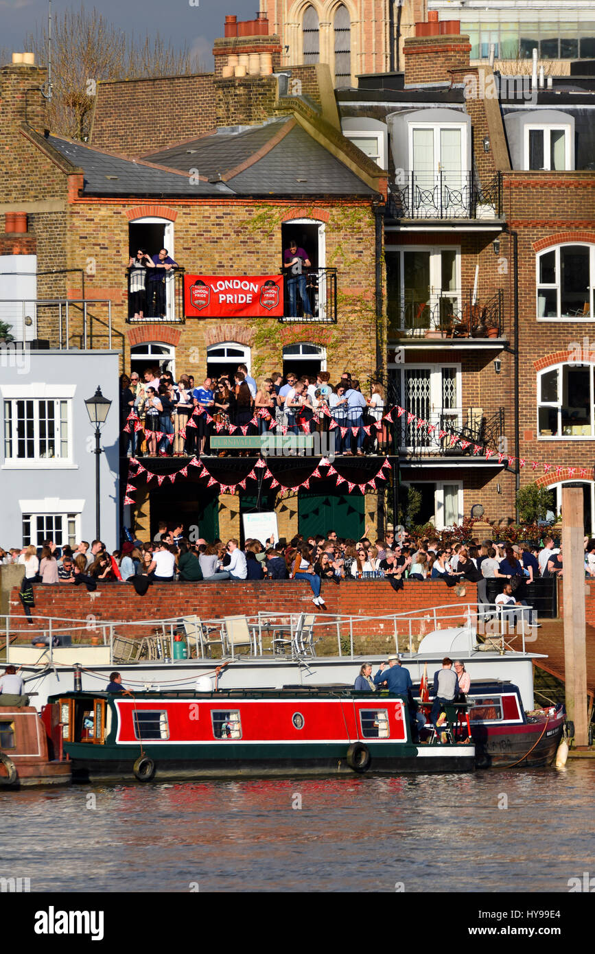 Menschenmassen, Menschen, die darauf warteten, die Universität Boot Rennen auf der Themse bei Barnes, London zu sehen. Riverside Pub. Trinker Stockfoto