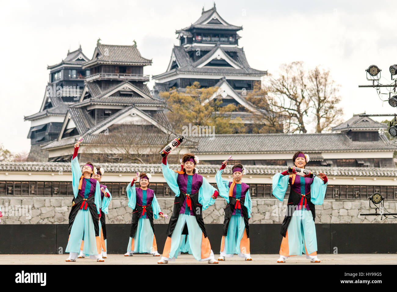 Hinokuni Yosakoi Dance Festival in Japan. Team von Reife Frauen tanzen auf der Bühne in Schwarz und Türkis Kostüm mit Kumamoto Schloss im Hintergrund. Stockfoto