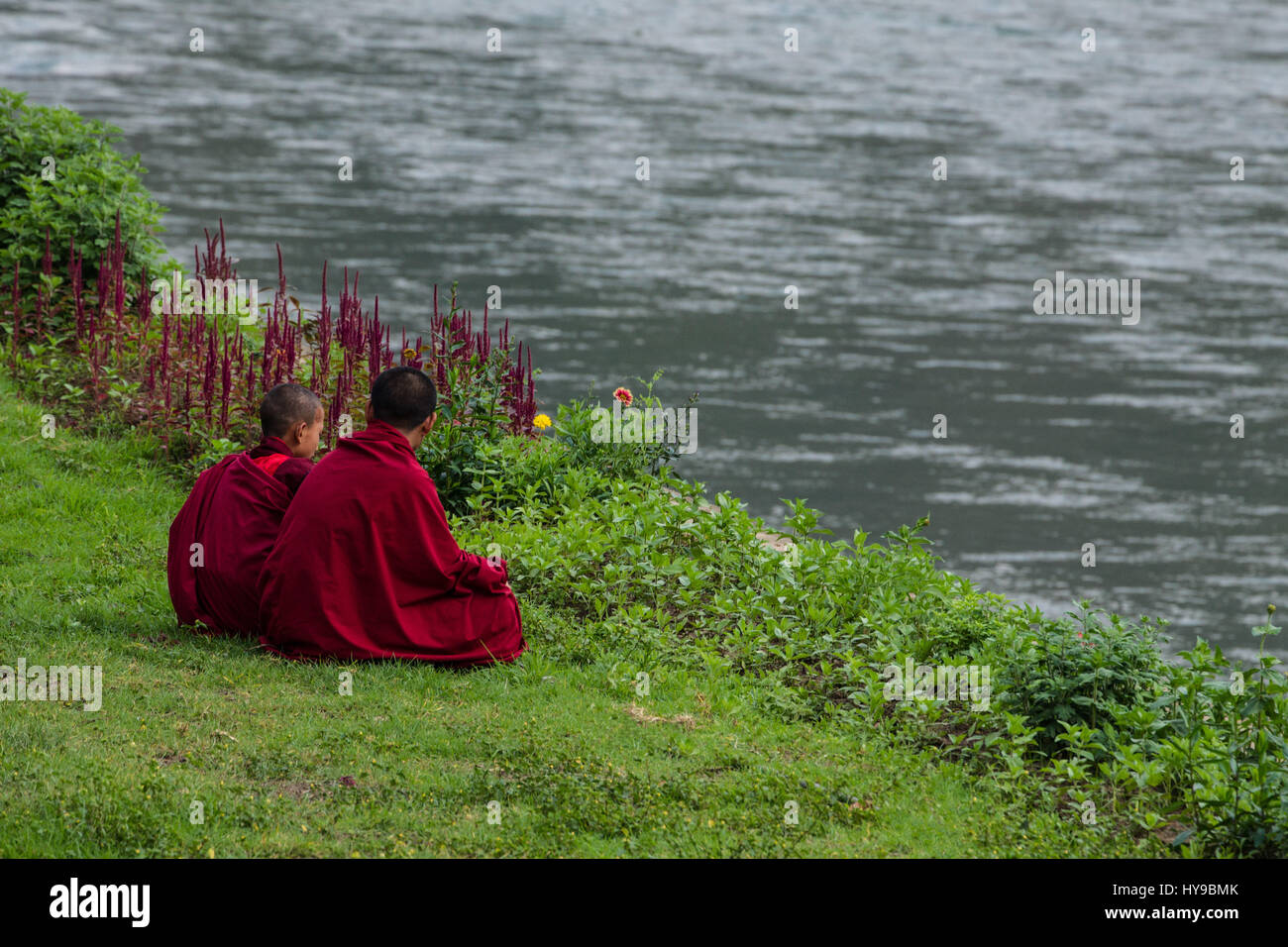 Zwei junge Novizin buddhistische Mönche sitzen auf der Wiese am Ufer des Flusses Mo Chhu in Punakha Dzong in Punakha, Bhutan. Stockfoto