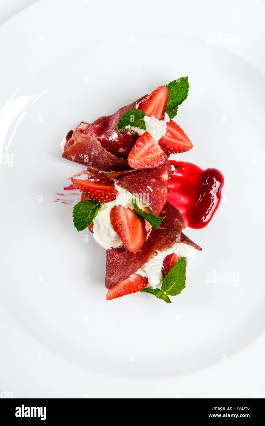 Erdbeeren und Minze in weiße Creme mit in Scheiben geschnittenen Schinken bedeckt. Stockfoto