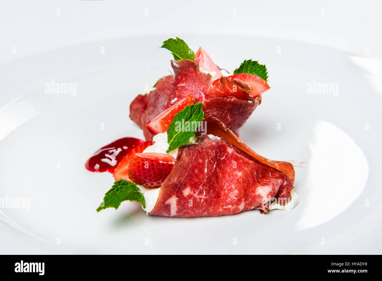 Erdbeeren und Minze in weiße Creme mit in Scheiben geschnittenen Schinken bedeckt. Stockfoto