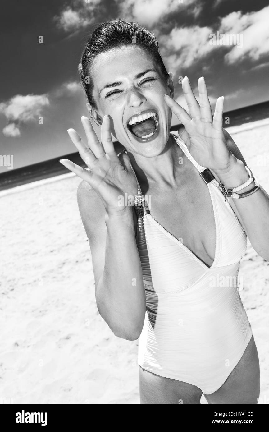 In Richtung zum weißen Sand Meer-Paradies. Glückliche Frau in weißen Badeanzug durch Megaphon schreien geformte Hände am Sandstrand an einem sonnigen Tag Stockfoto