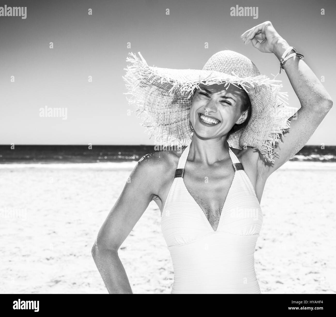 In Richtung zum weißen Sand Meer-Paradies. Porträt der glückliche Frau in weißen Badeanzug und Strohhut am Sandstrand an einem sonnigen Tag Stockfoto