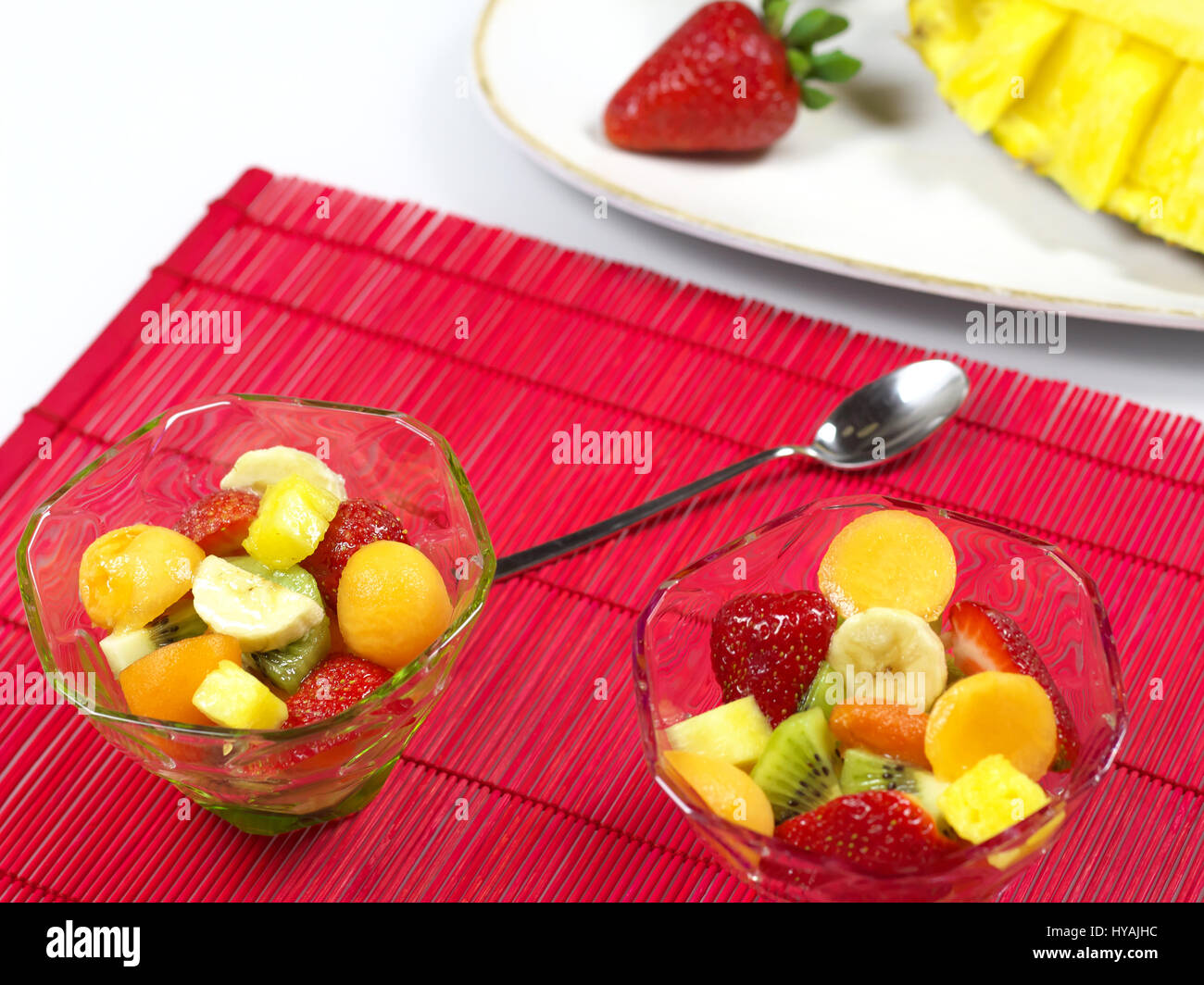 Obstsalat mit Erdbeeren, Melone, Kiwi, Banane und Ananas in Klarglas Cups  (Schalen) mit einem Teelöffel auf rote Platzdeckchen auf weißen Tisch  serviert Stockfotografie - Alamy