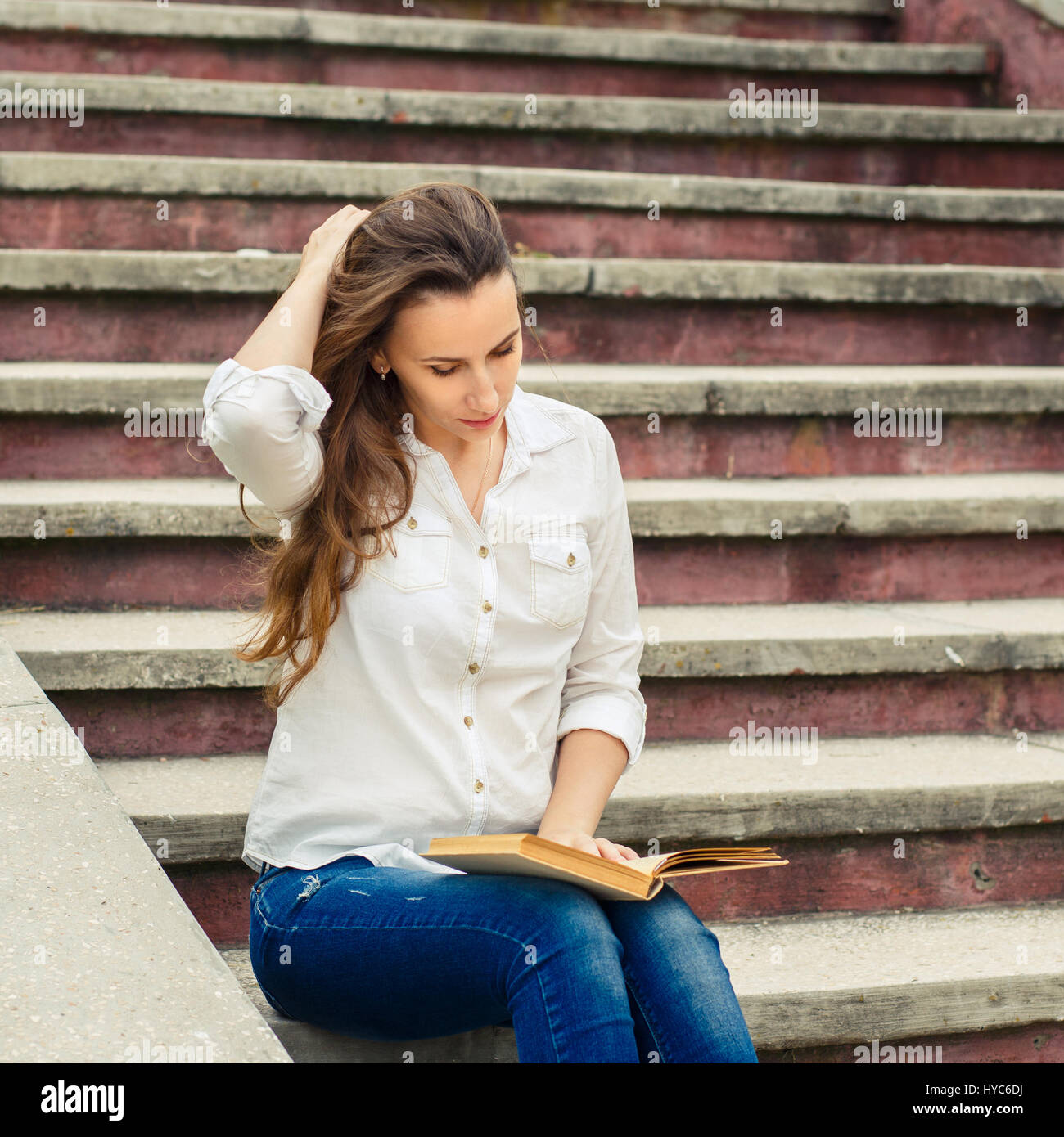 Junge Frau sitzt auf der Treppe mit Buch. Hispanischen Mädchen Lesebuch im Freien. Getönten Bild Stockfoto