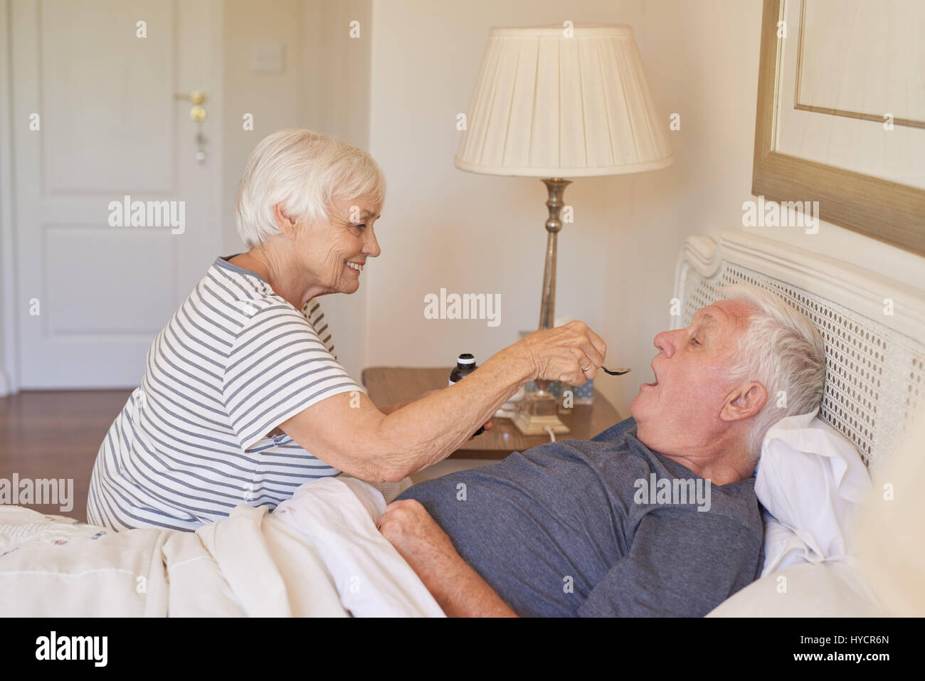 Ältere Frau, die Medizin zu ihrem kranken Mann im Bett zu geben Stockfoto