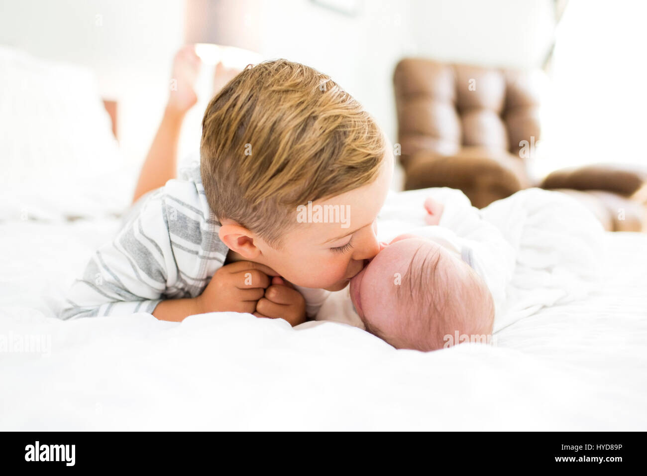 Bruder (4-5) auf dem Bett liegend und küssende Schwester (0-1 Monate) Stockfoto