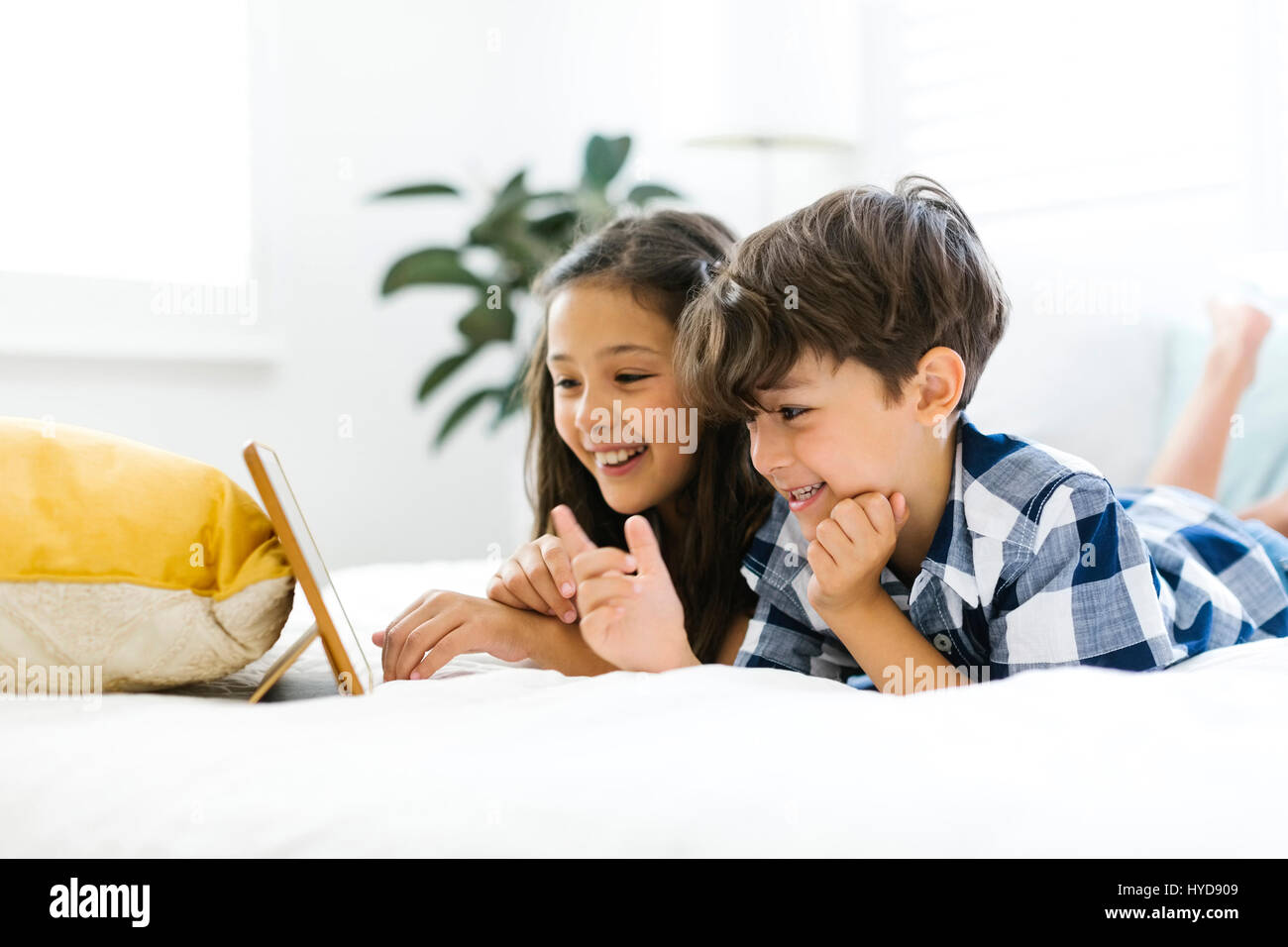 Geschwister (10-11, 6-7) liegen im Bett und benutzen Tablet Stockfoto