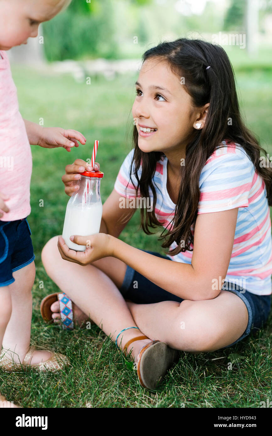 Mädchen (10-11) teilen Flasche Milch mit Schwester (2-3) in parken Stockfoto