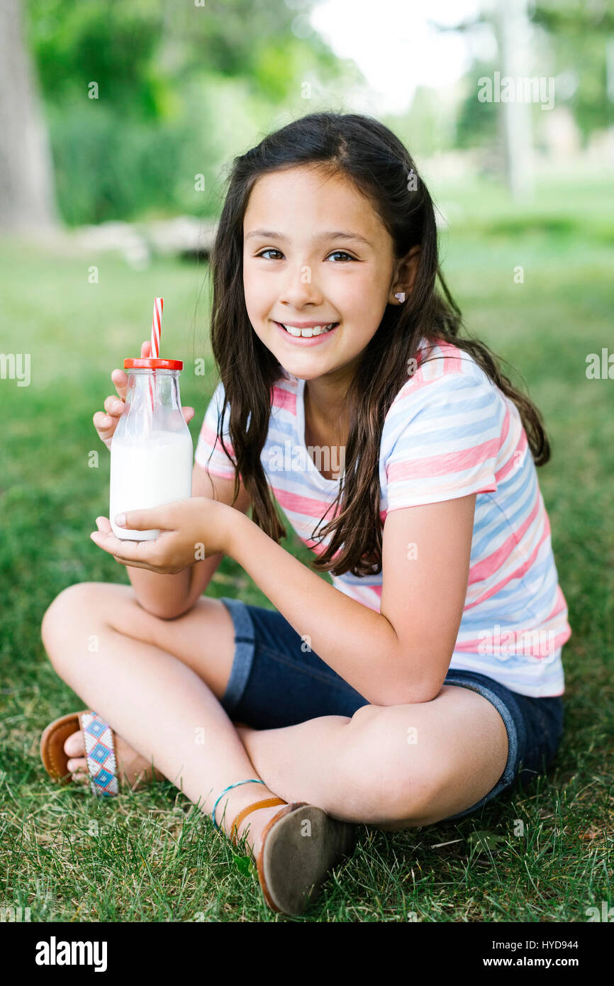 Mädchen (10-11) sitzt auf Gras mit einem Glas Milch Stockfoto