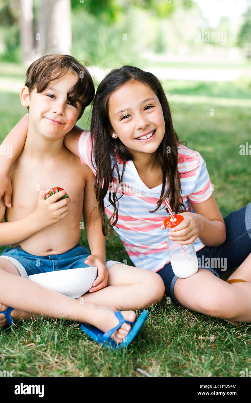 Junge (6-7) und Mädchen (10-11) sitzen im Sommer auf Gras Stockfoto