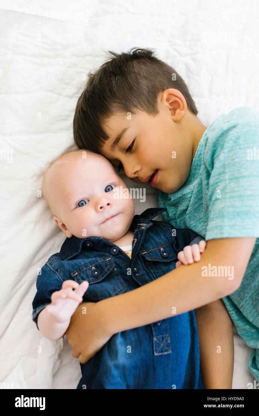 Zwei Brüder (6-11 Monate) liegen auf dem Bett und umarmen Stockfoto Zwei Brüder (6-11 Monate) liegen auf dem Bett und umarmen Stockfoto