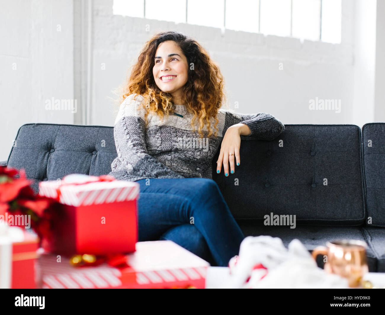 Glückliche Frau auf Sofa mit Weihnachtsgeschenken im Vordergrund Stockfoto