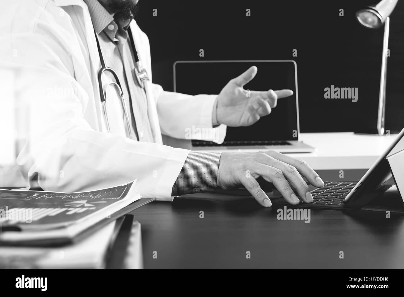 Medizintechnik-Konzept. Arzt arbeitet mit Smartphone und Stethoskop und digitale Tablettcomputer in modernen Büro im Krankenhaus, schwarz / weiß Stockfoto