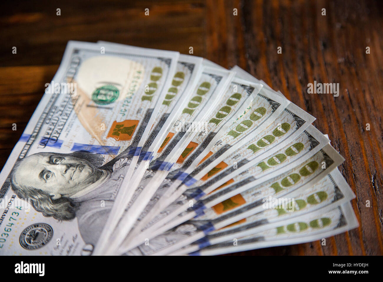 Ein Stapel von ganz neuen Hundert-Euro-Scheine in US-Währung schwärmten aus, auf einem dunkelbraunen hölzernen Tisch Stockfoto