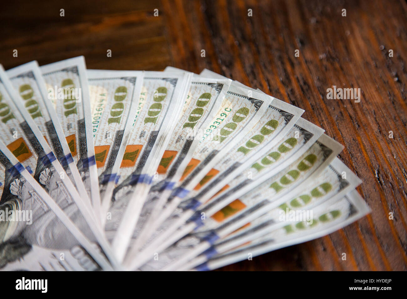 Ein Stapel von ganz neuen Hundert-Euro-Scheine in US-Währung schwärmten aus, auf einem dunkelbraunen hölzernen Tisch Stockfoto