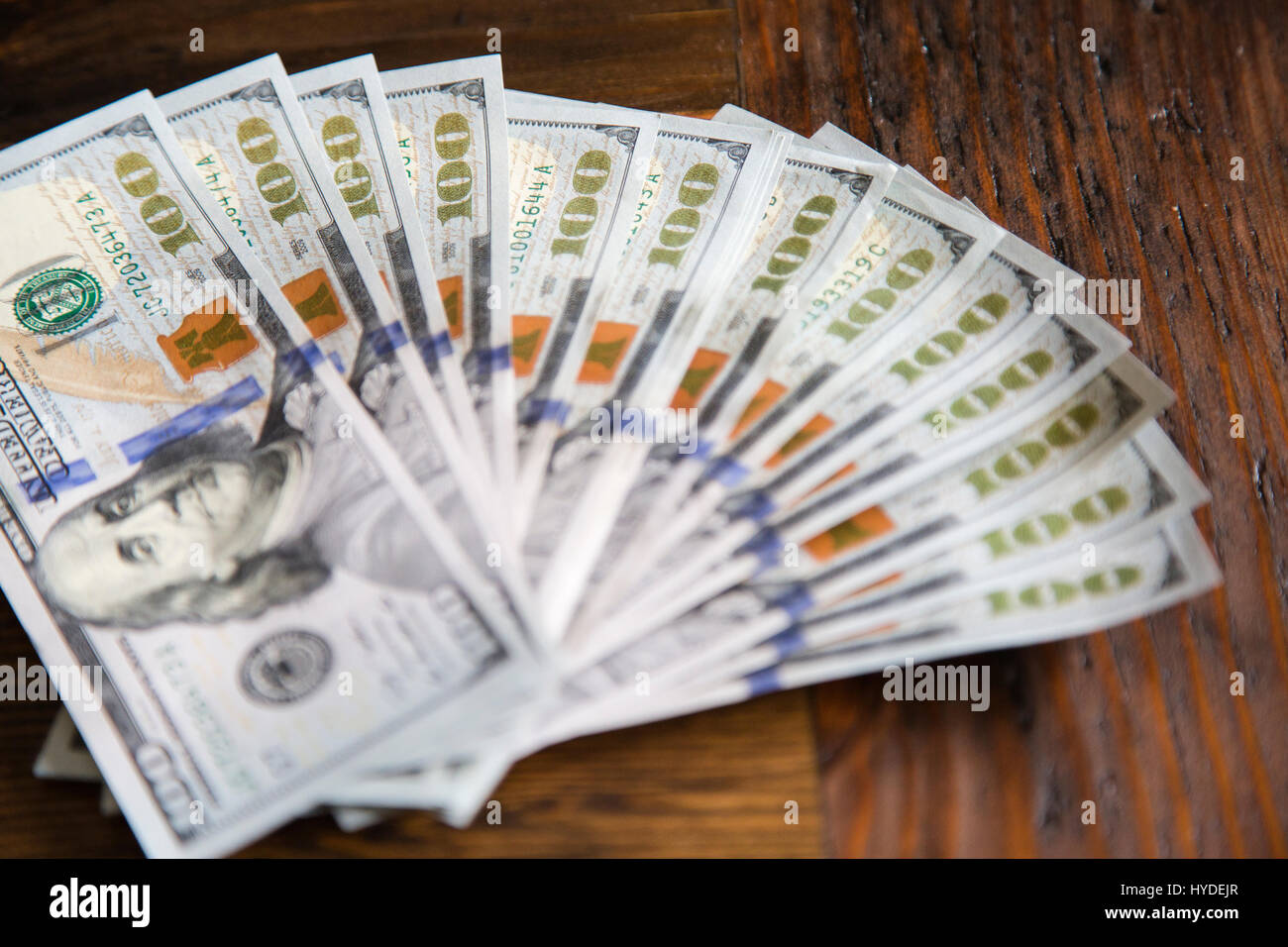 Ein Stapel von ganz neuen Hundert-Euro-Scheine in US-Währung schwärmten aus, auf einem dunkelbraunen hölzernen Tisch Stockfoto