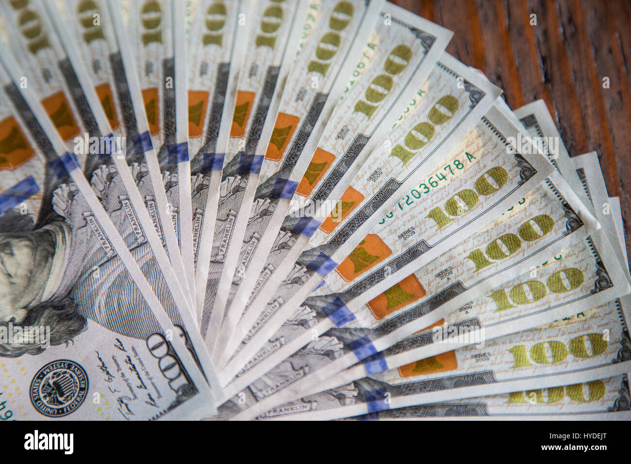 Ein Stapel von ganz neuen Hundert-Euro-Scheine in US-Währung schwärmten aus, auf einem dunkelbraunen hölzernen Tisch Stockfoto