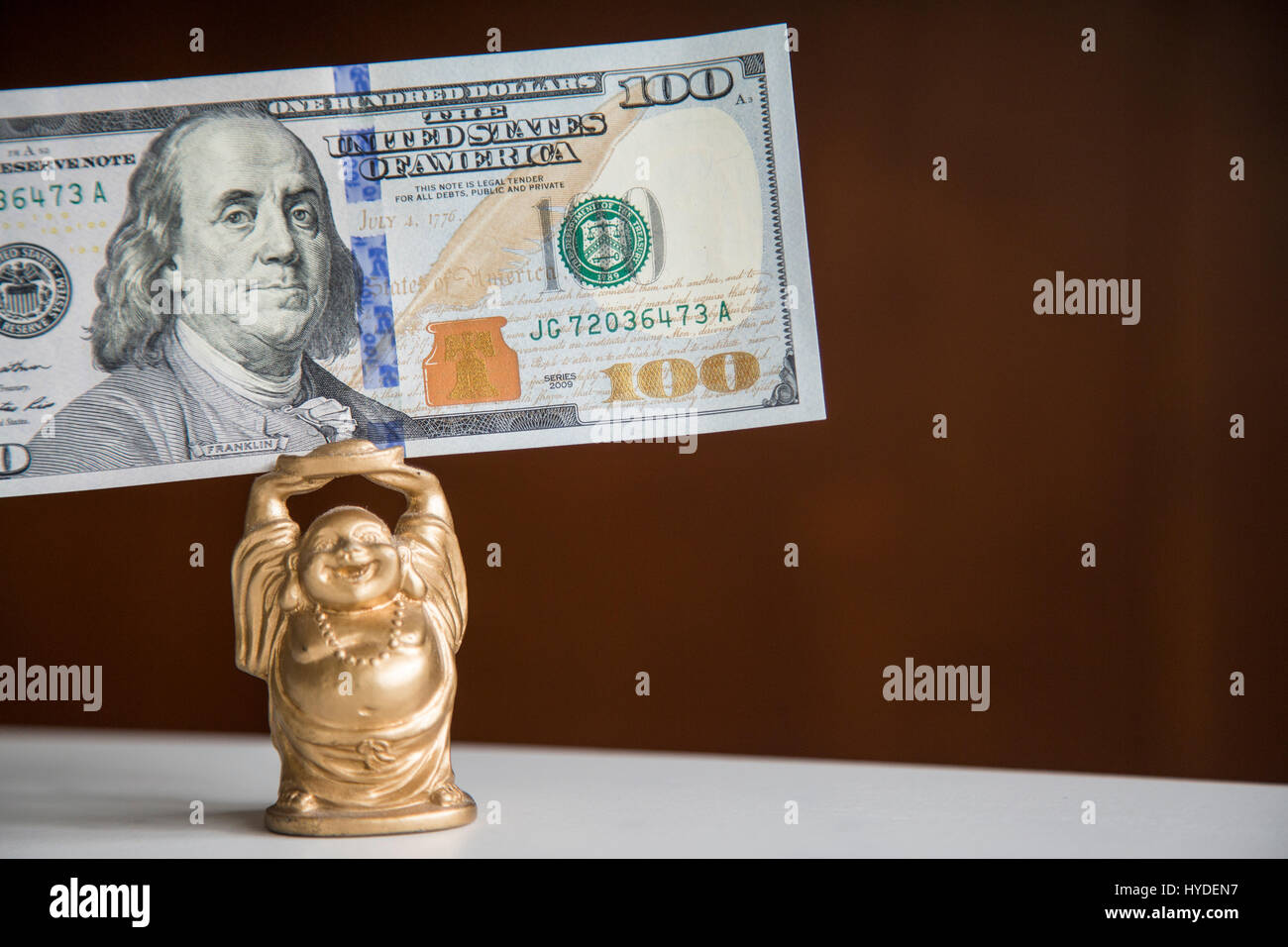 Eine kleine goldene Buddha Figur hält ein Hundert Dollar Bill der US-Währung über seinem Kopf Stockfoto