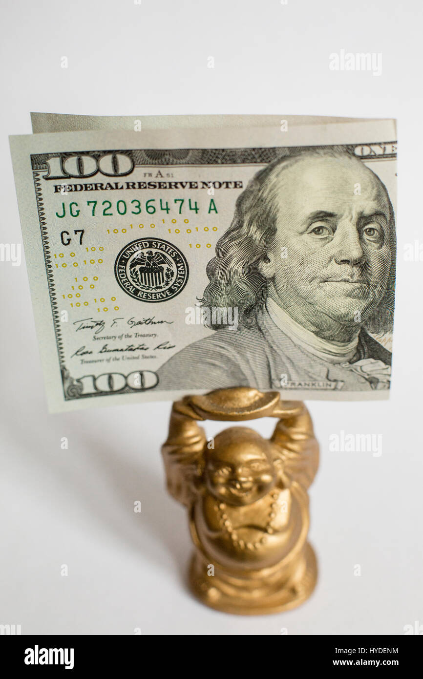 Eine kleine goldene Buddha Figur hält ein Hundert Dollar Bill der US-Währung über seinem Kopf Stockfoto