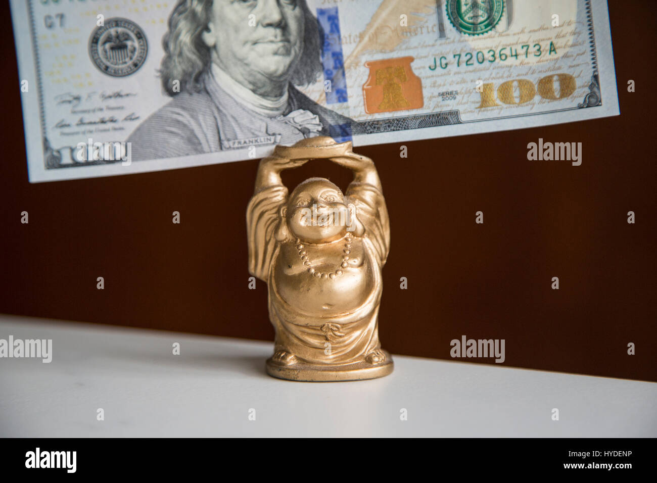 Eine kleine goldene Buddha Figur hält ein Hundert Dollar Bill der US-Währung über seinem Kopf Stockfoto