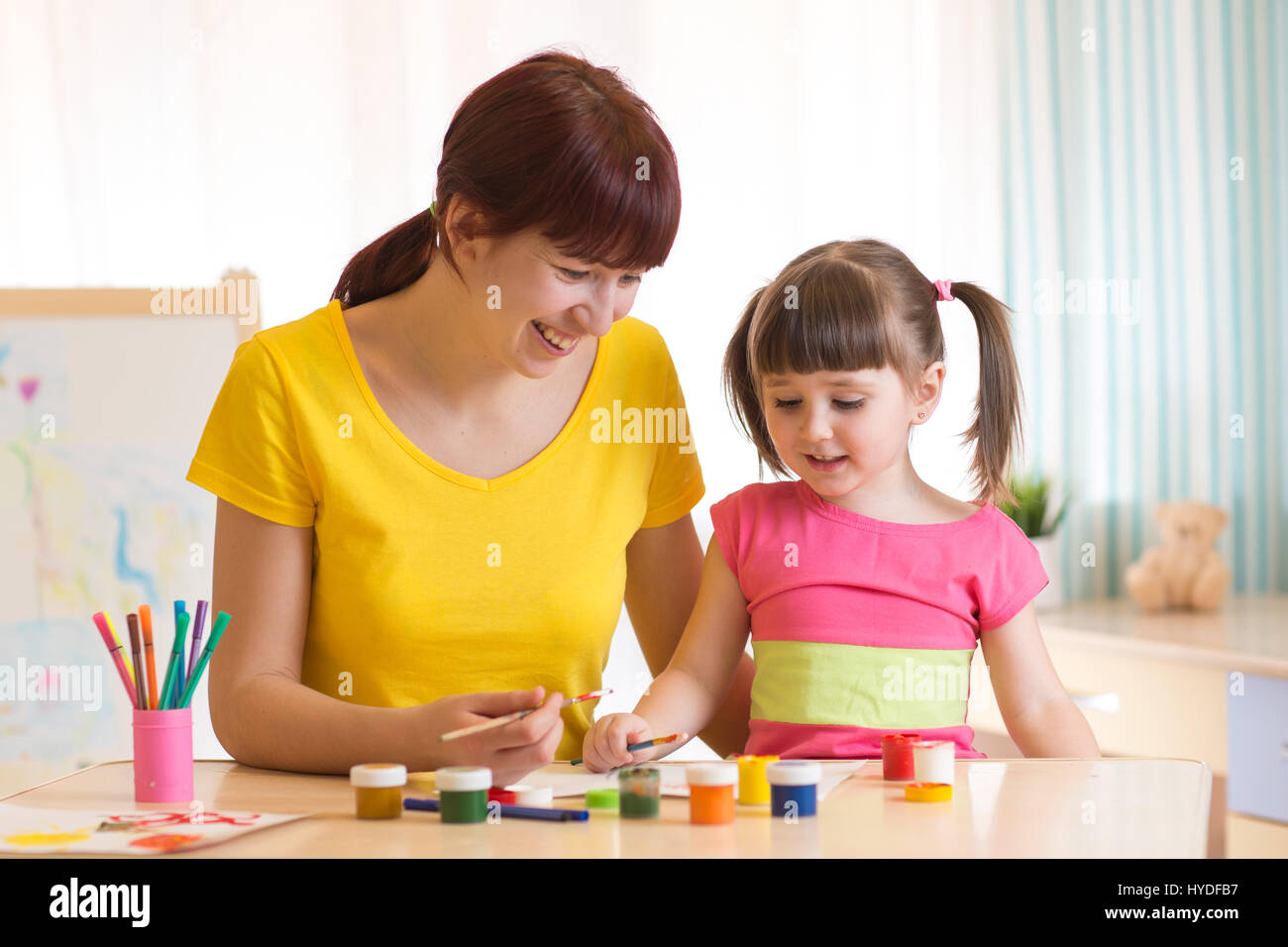 Glückliche Familie Mutter und Kind Tochter malen zusammen. Erwachsene Frau hilft Kind Mädchen. Stockfoto