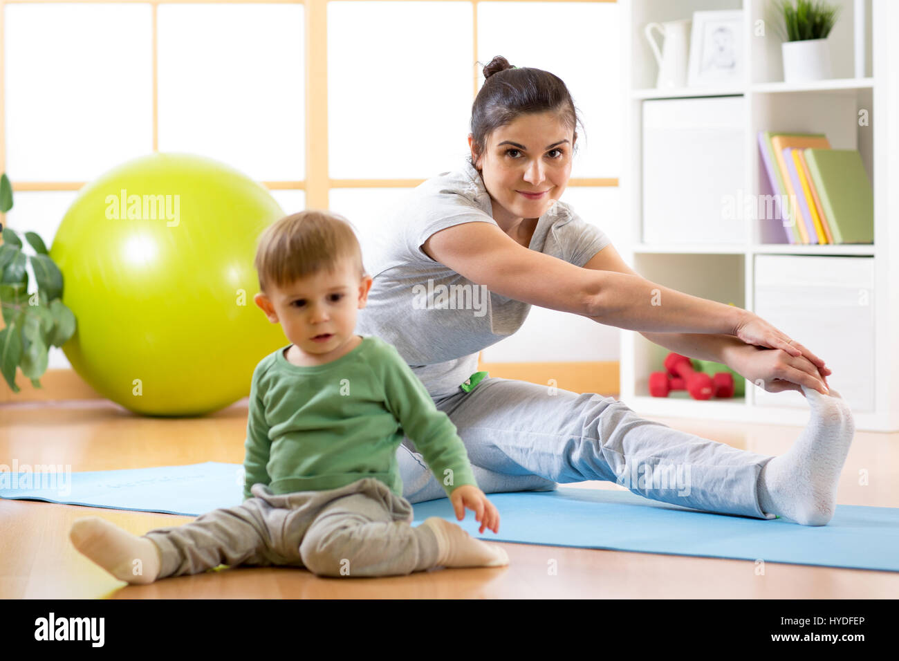 Sportliche Frau beschäftigt sich mit Fitness und Yoga zu Hause. Ihr Sohn Kind von in der Nähe von sitzen und spielen. Stockfoto