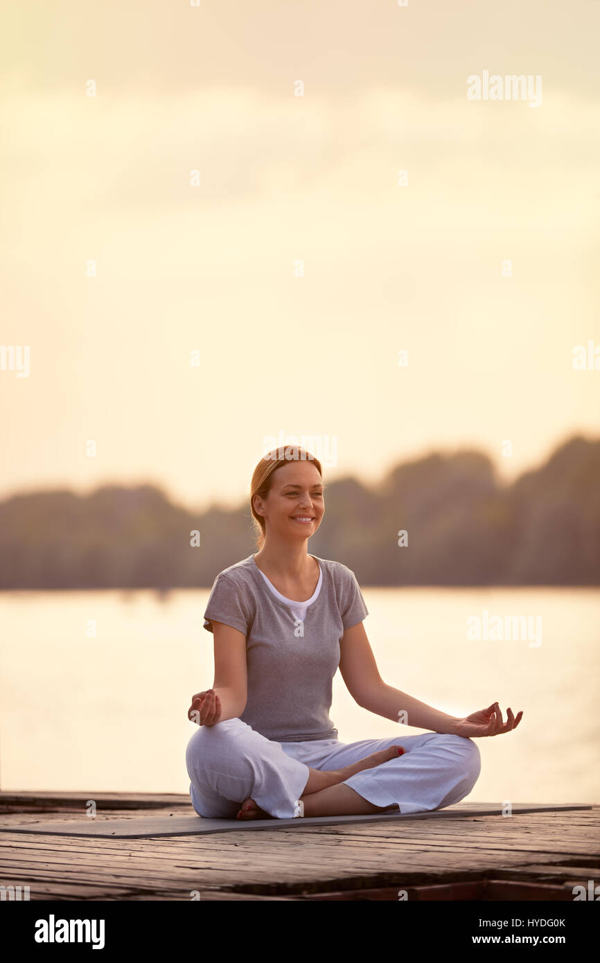 Lächelnde weibliche Person am Fluss in Yoga-pose Stockfoto