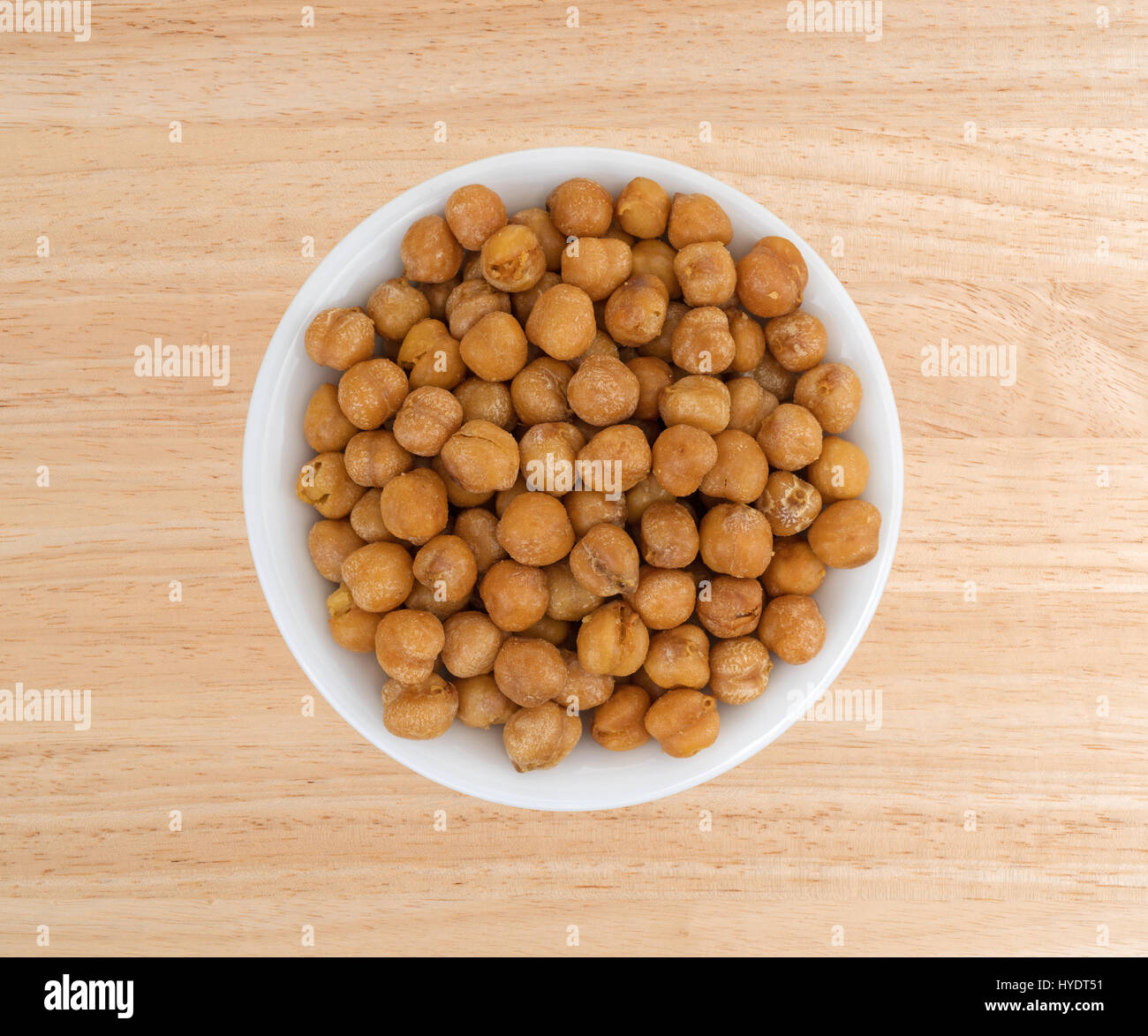 Draufsicht auf eine Portion geröstete Kichererbsen mit Meersalz in einer kleinen weißen Schüssel auf einem Holztisch. Stockfoto