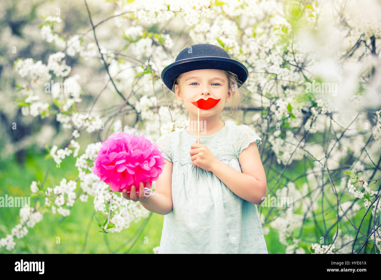 Lustiges Mädchen mit Hut und mit gefälschten Lippen im Frühlingsgarten. Stockfoto