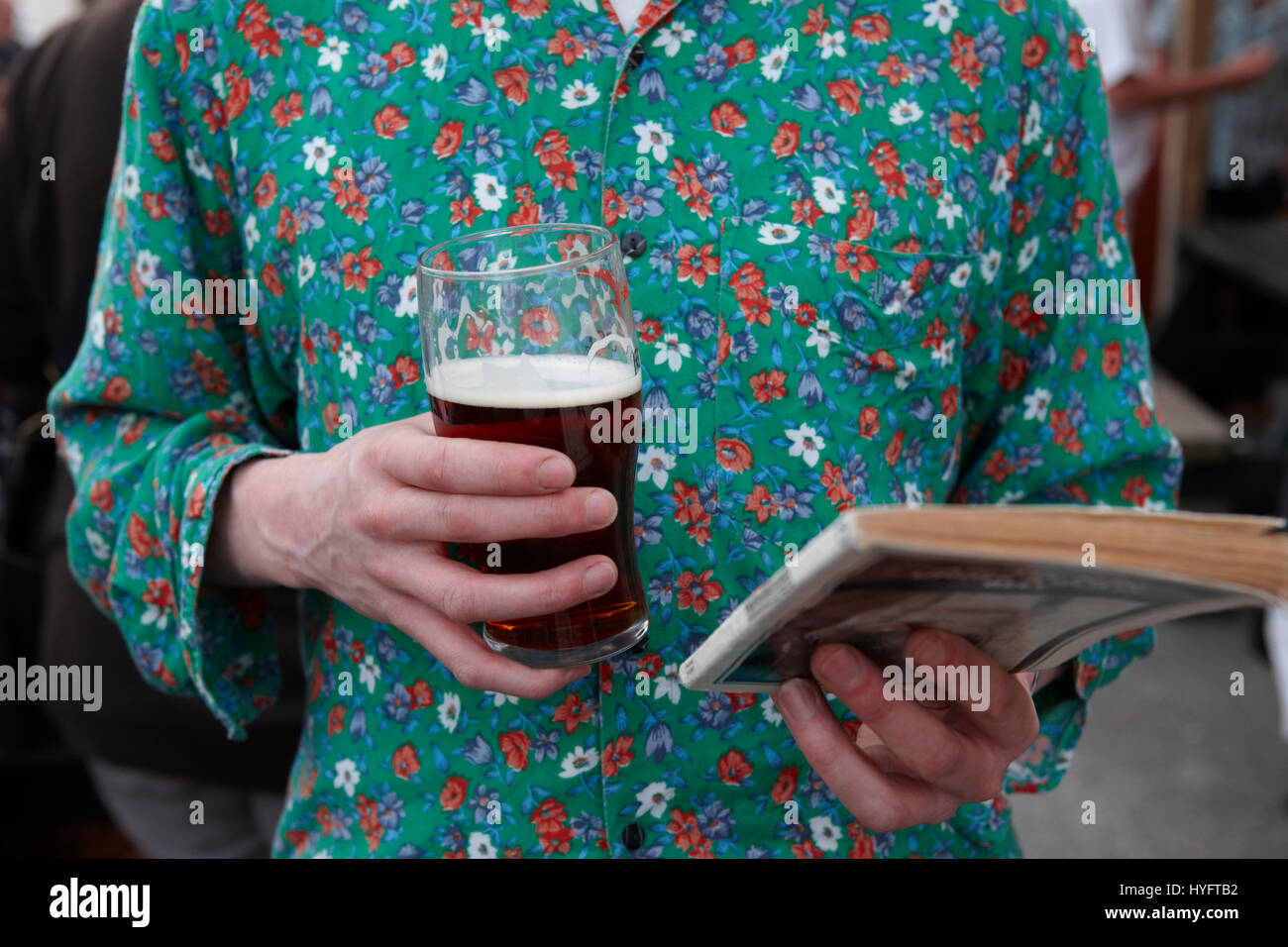 Ein Mann trägt einen grünen blumigen Top, ein Buch zu lesen, hält einen Pint im The Literary Festival, Laugharne, Wales, Uk Stockfoto