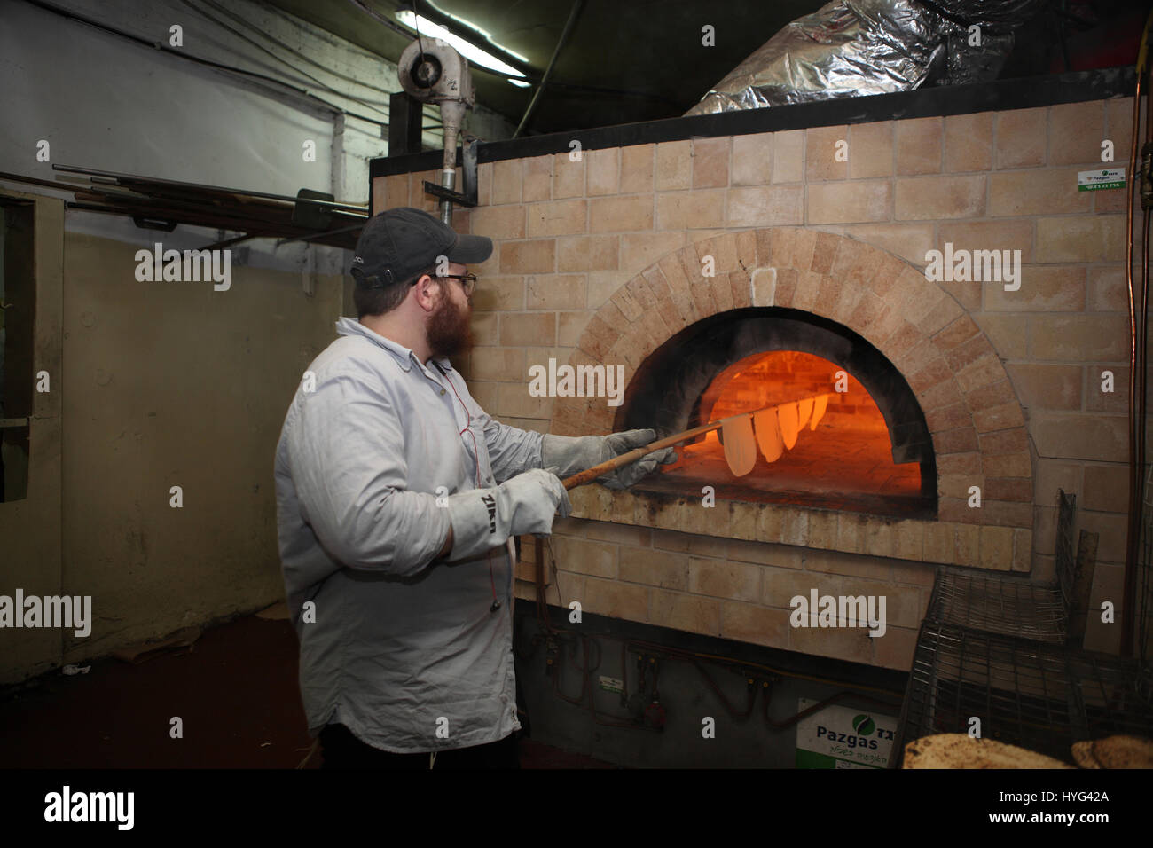 Ein chassidische Mann verwendet einen langen Stock, abgeflachte Stücke der Teig im Ofen backen Matza oder Matzah Shmura für Pessach in einer handgefertigten Matza-Fabrik Stockfoto