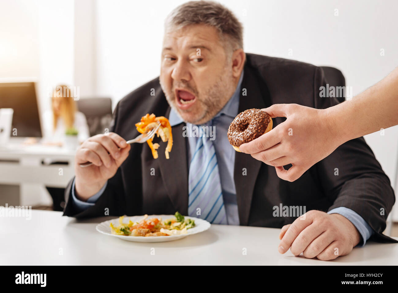 Grausame Kollegen necken übergewichtigen Mann mit Süßigkeiten Stockfoto