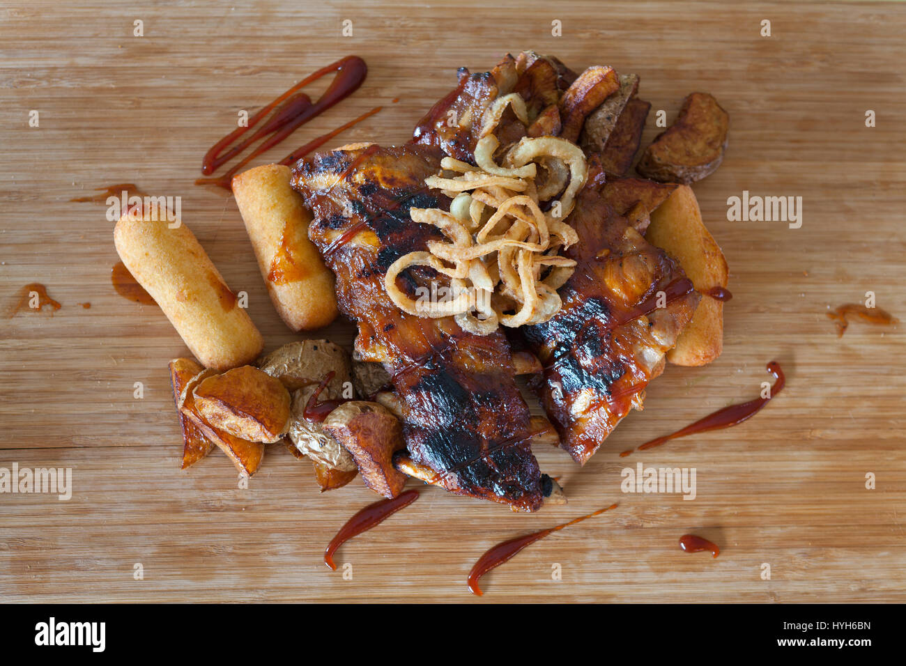 Amerikanische gegrillte Rippchen auf dem Grill mit Barbecue-Sauce mit Zwiebelringen garniert und heißen knusprigen Kartoffeln mit gestampften Kartoffeln gefüllte Kroketten - American Stockfoto