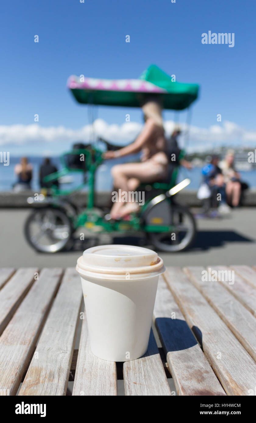 Ein Kunststoff Kaffeetasse auf einem Holztisch mit unscharfen Personen im Freien. Stockfoto