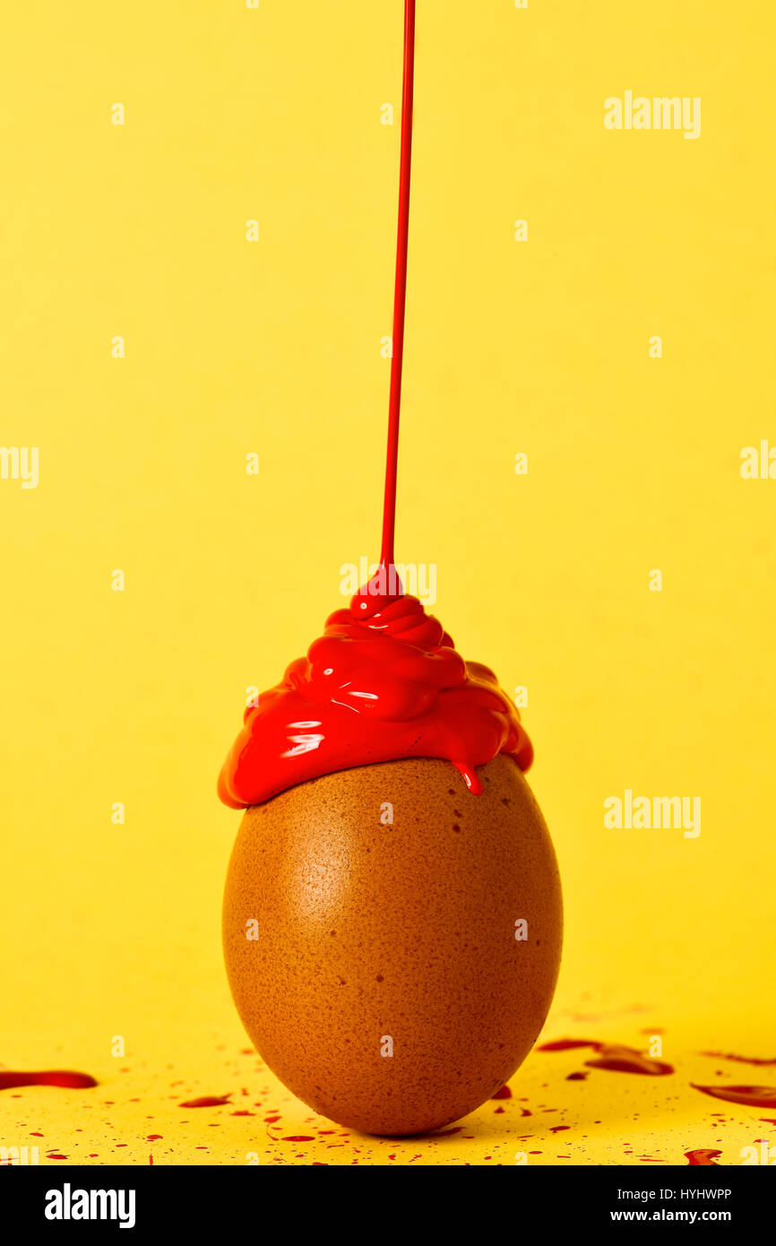 roter Farbe auf einem braunen Ei fallen platziert auf einem gelben Hintergrund von der gleichen Farbe bespritzt Stockfoto