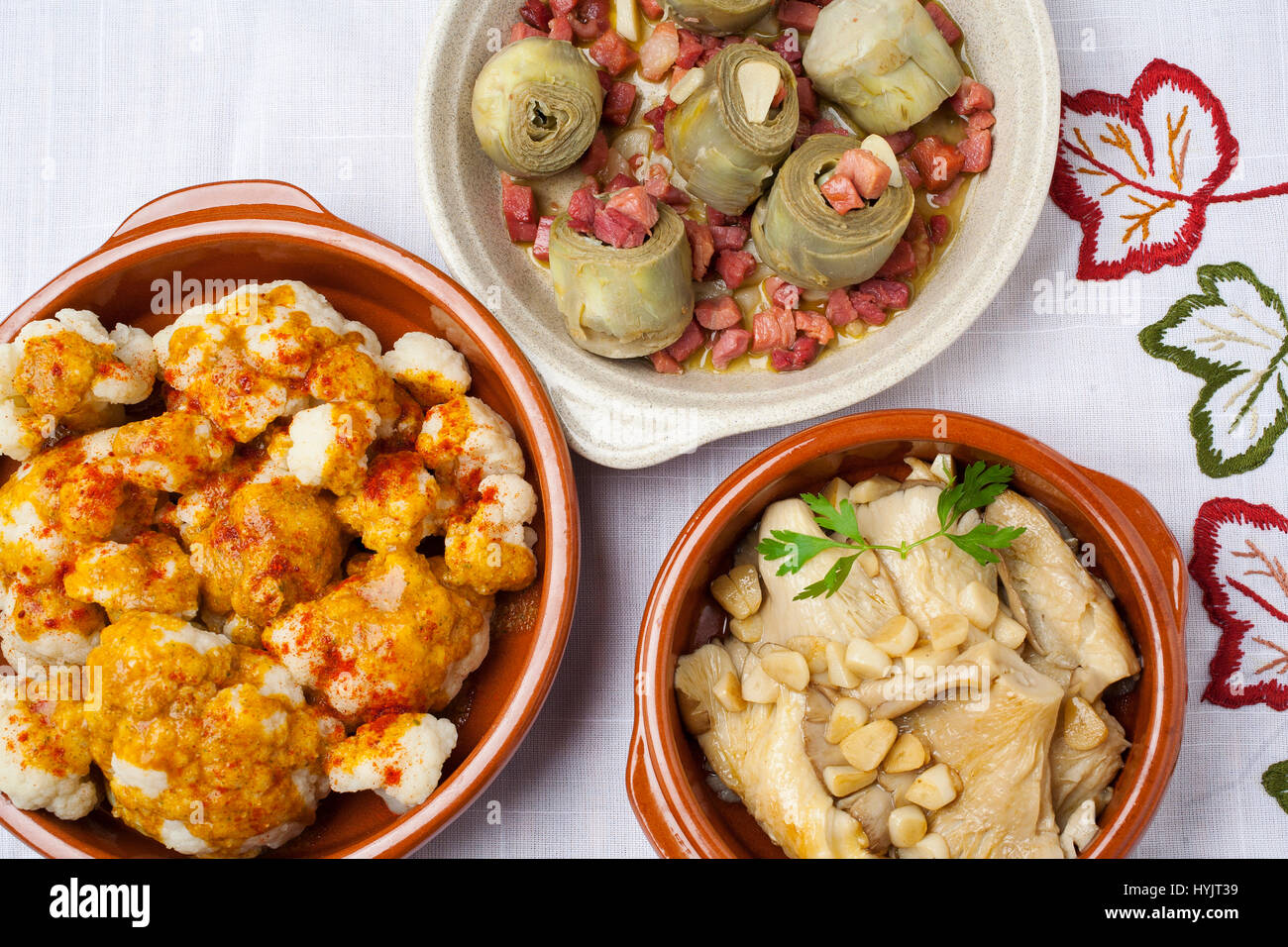 Tapas essen. Traditionelle Gerichte der spanischen Gastronomie. Blumenkohl mit Pimentón, Artischocken mit Schinken und Champignons mit Knoblauch Stockfoto