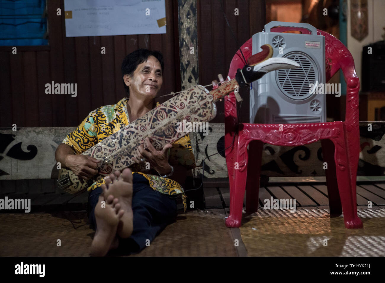 Ein Mann, der im Bali Gundi Longhouse in Kapuas Hulu, West Kalimantan, Indonesien, „Lampe“ (sape), ein traditionelles Saiteninstrument aus Dayaknese, spielt. Stockfoto