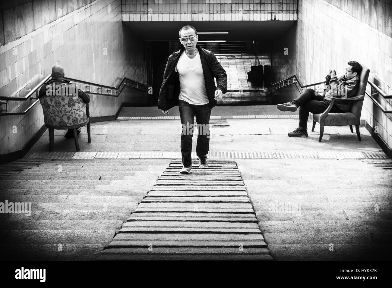Schwarz / weiß Bild der Platz des himmlischen Friedens Unterführung mit ein asiatischer Mann zu Fuß und zwei Männer sitzen in bequemen Stühlen, Peking, China Stockfoto