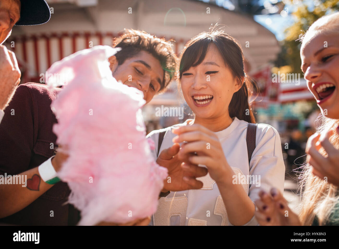 Gruppe von Freunden essen Zuckerwatte im Freizeitpark. Lächelnde junge Menschen teilen Zuckerwatte im Freien. Stockfoto