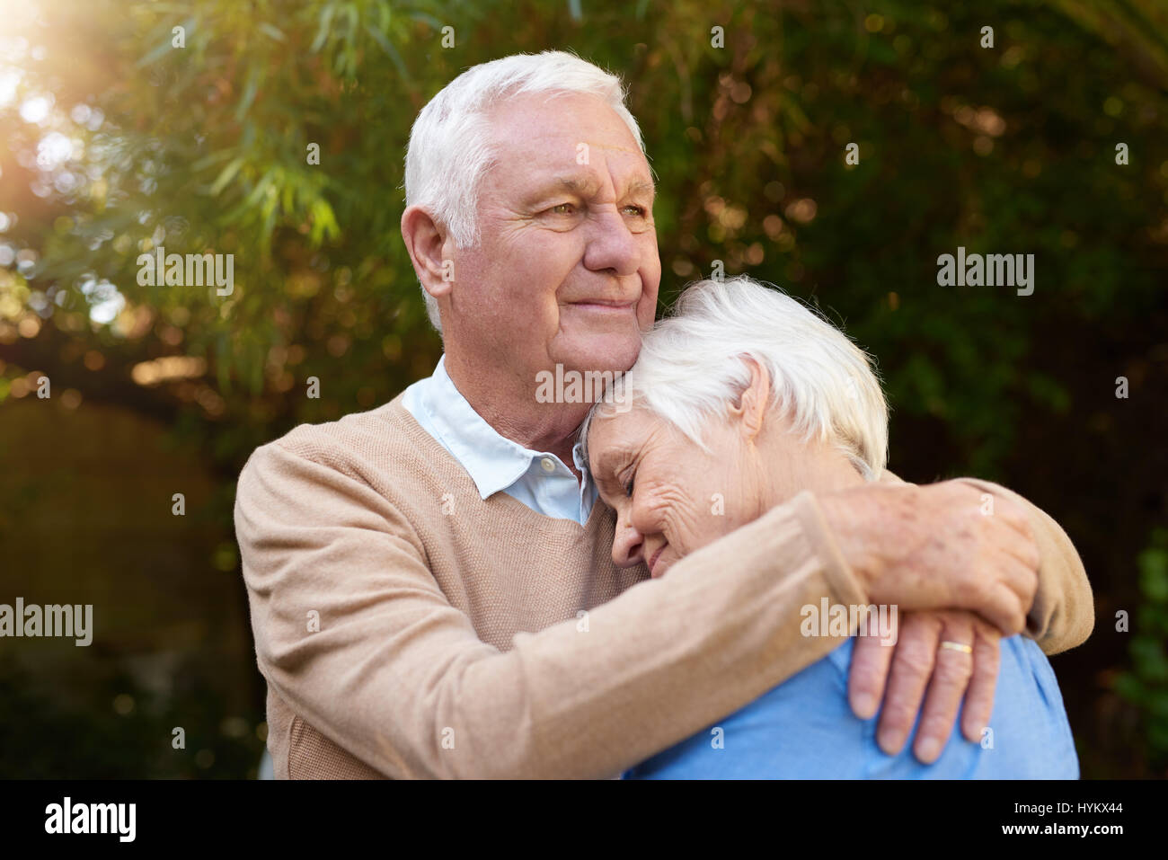 Lächelnd senior Mann liebevoll umarmt seine Frau draußen Stockfoto